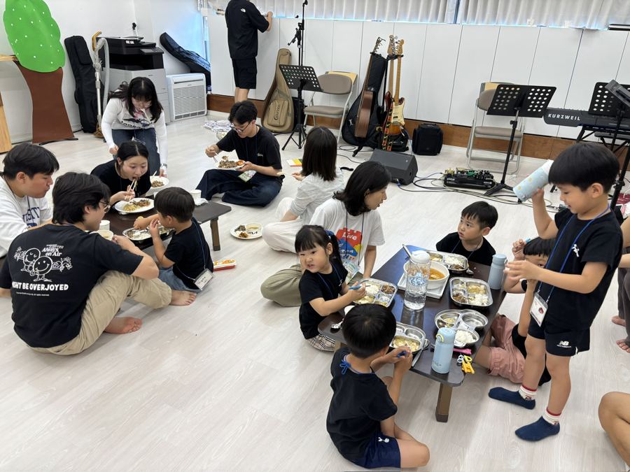 아이들과 청년들이 바닥에 둘러앉아 식사하는 모습